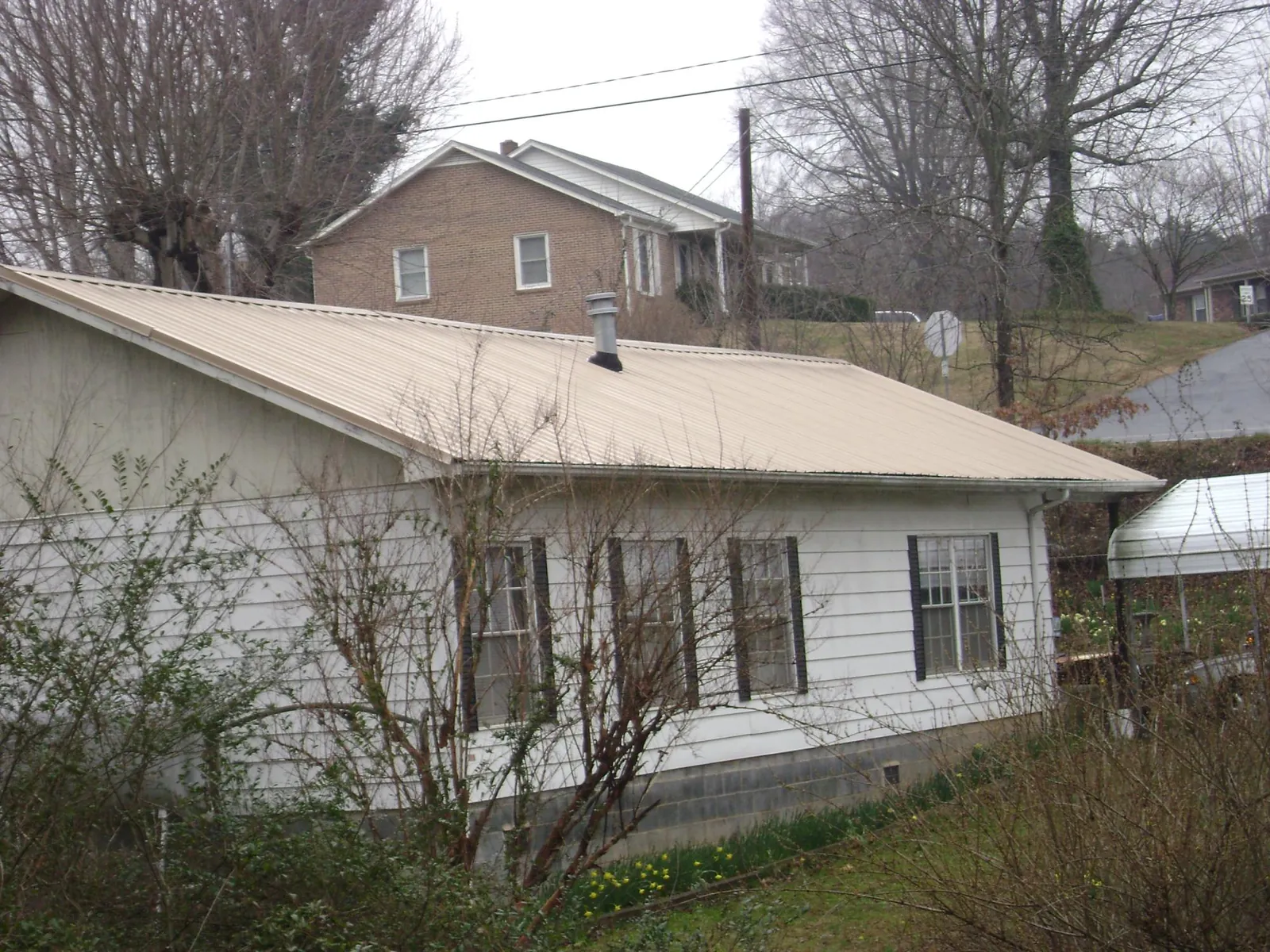 Tan metal roof on a white sided house set into a hillside — Commercial Roofing by Roofing Brothers in Beaumont