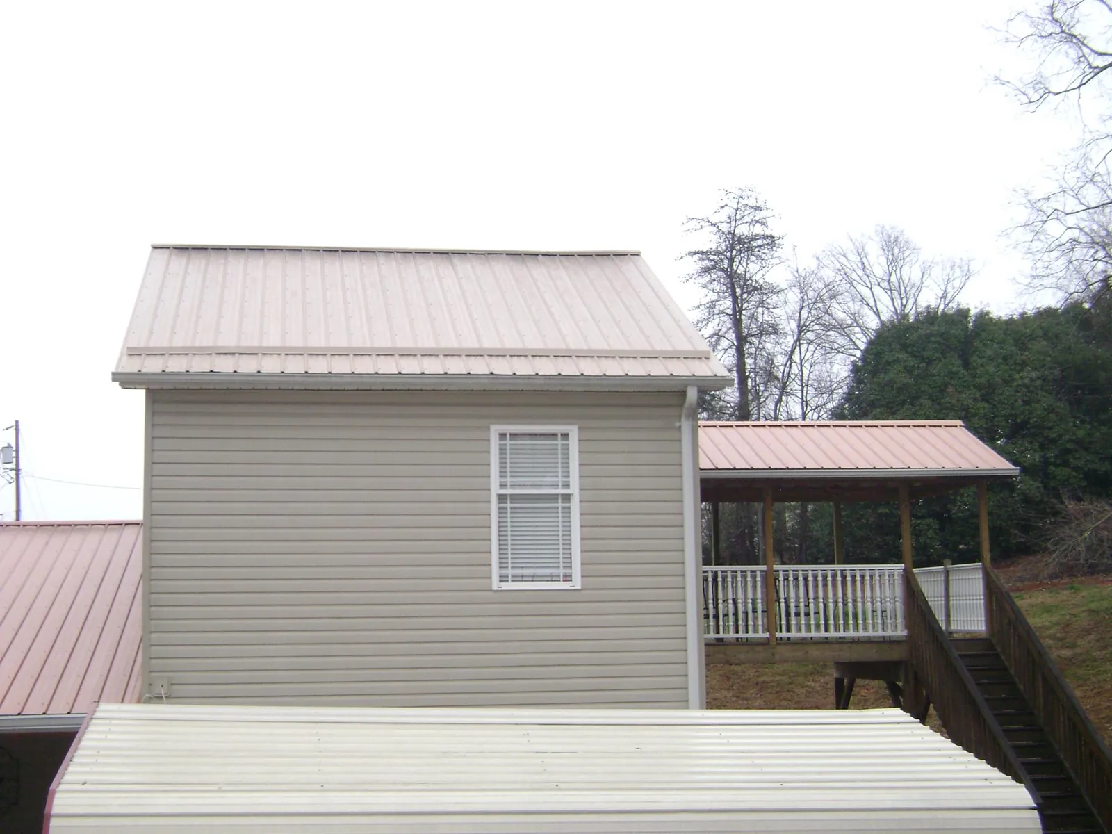 Tan metal roofs on a two story addition and attached porch, from a Roof Replacement job in Beaumont